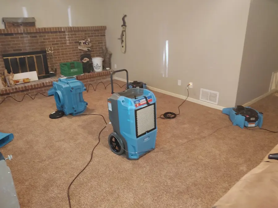 A dehumidifier and air movers drying a carpeted family room with a brick fireplace in Pueblo, CO