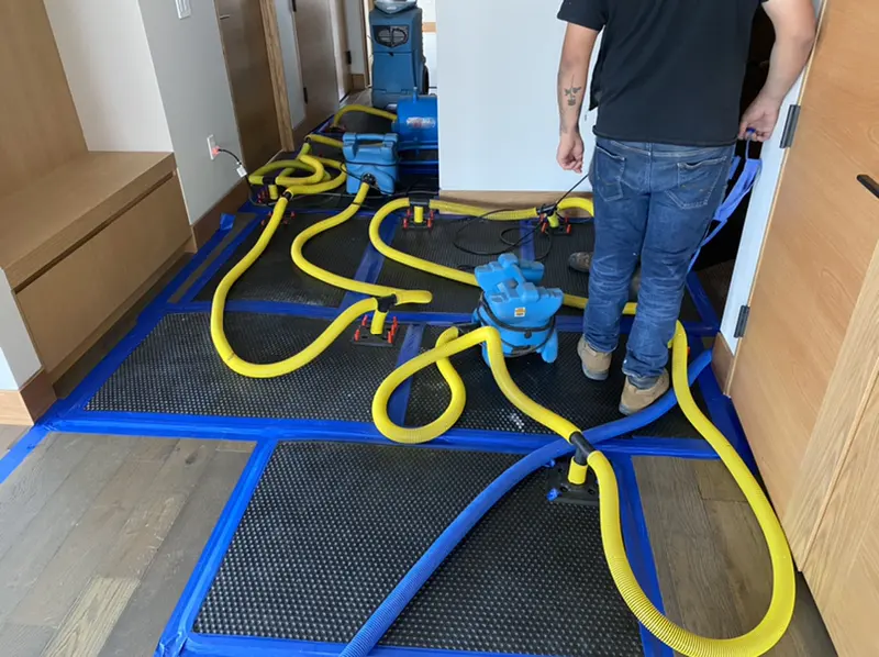 Hardwood floor drying mats connected by yellow hoses during structural drying in Pueblo, CO